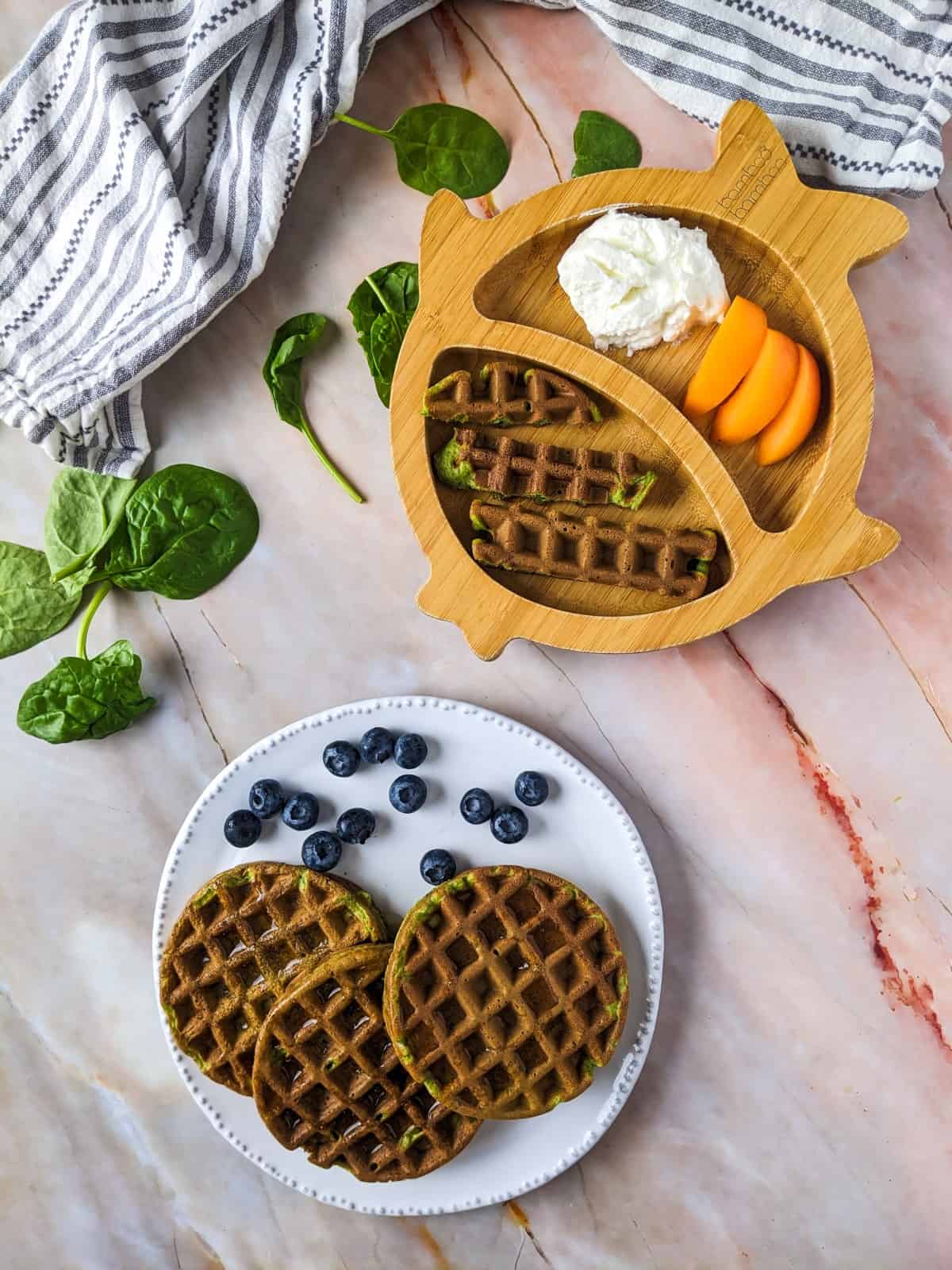 Spinach waffles served on white plate with blueberries and on bamboo plate for baby with yogurt and apricot slices.