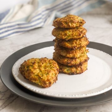 Zucchini fritters stack placed on a white plate.