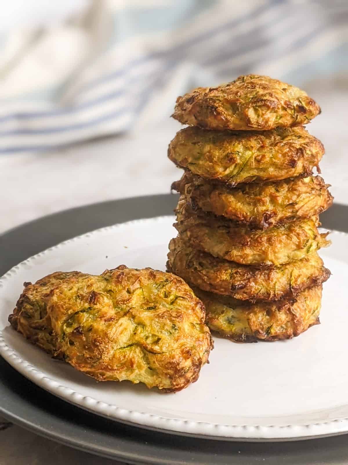 Zucchini fritters placed as a stack on a white plate.