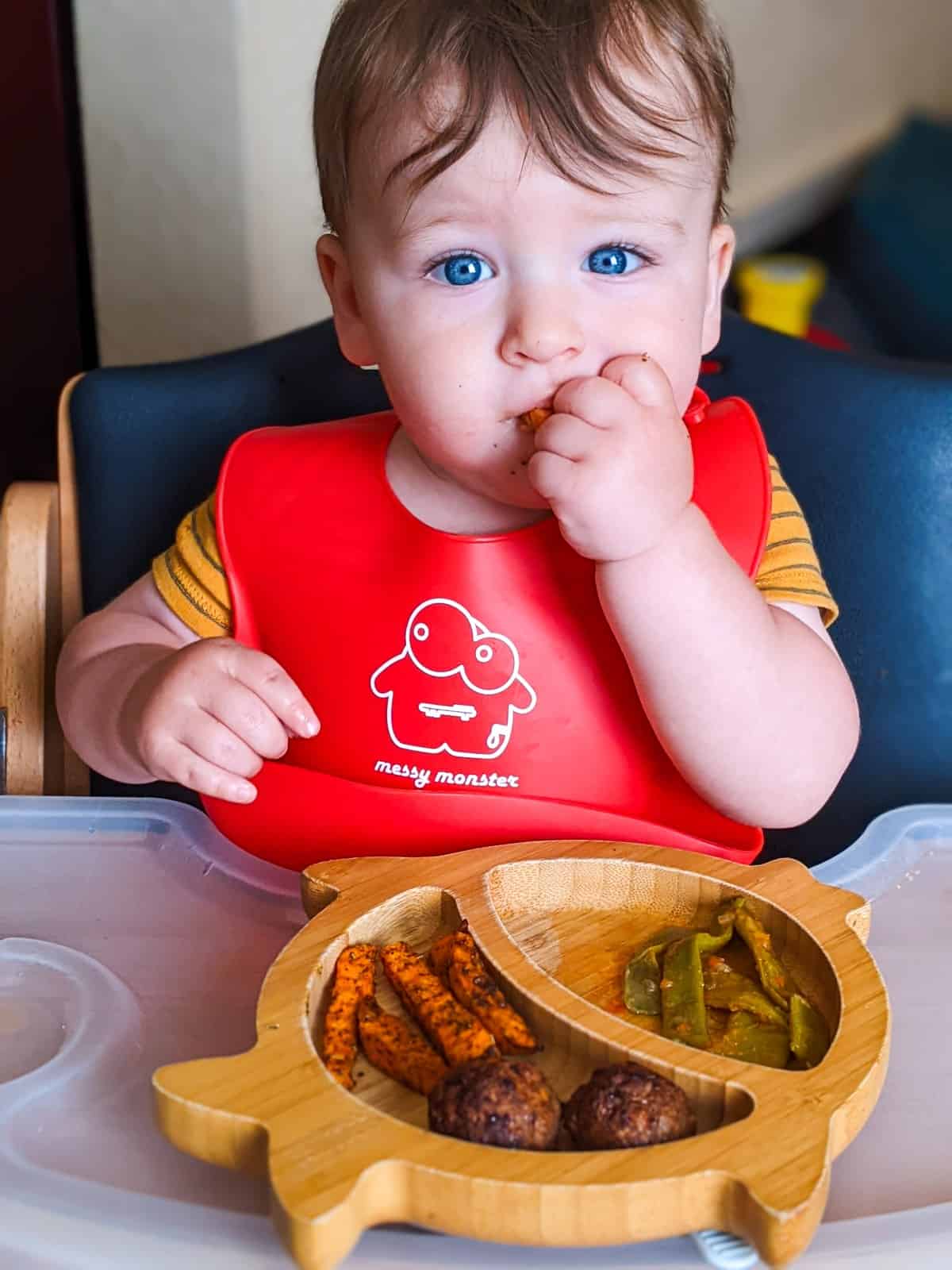 Baby following the BLW method and eating sweet potato on his highchair.