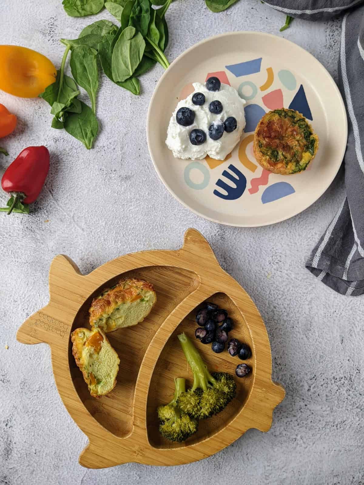 Egg muffins served on bamboo plate for baby with broccoli and blueberries and for toddler with yogurt and blueberries.