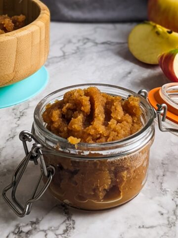 Homemade sugar-free applesauce in jar next to apples and wooden bowl.