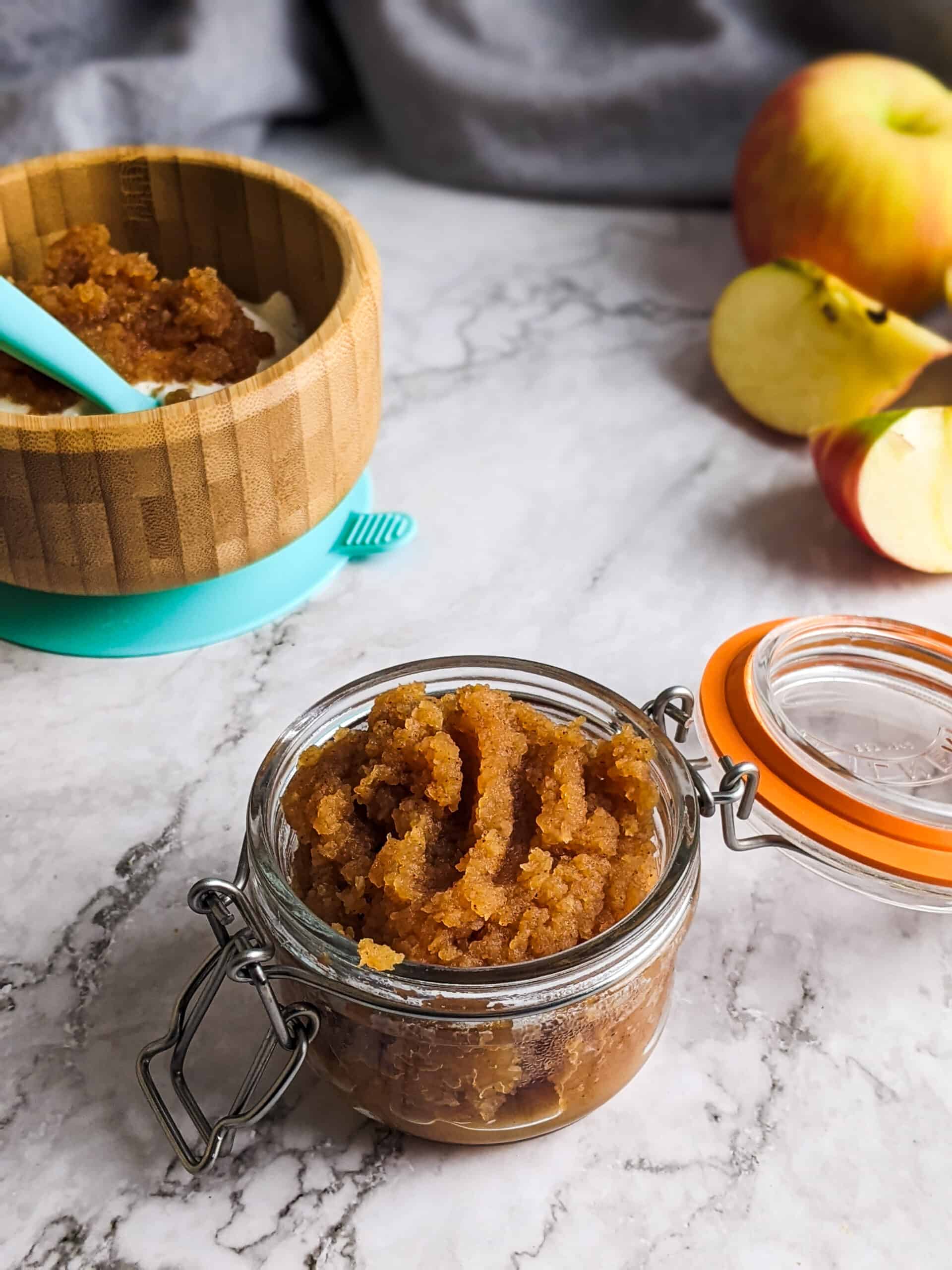 Homemade sugar-free applesauce in a jar with apples in a background and a bowl with yogurt and applesauce.