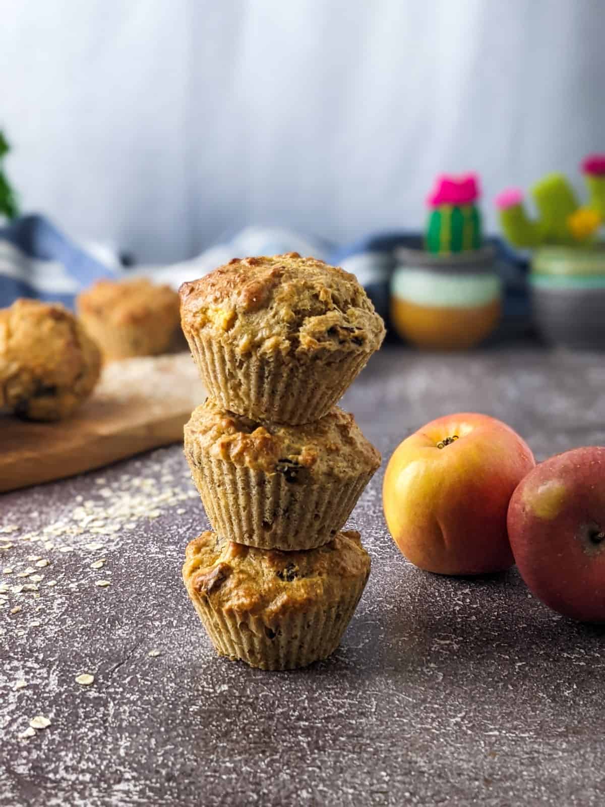 Three sugar-free apple muffins stack on top of each other with apples next to them.