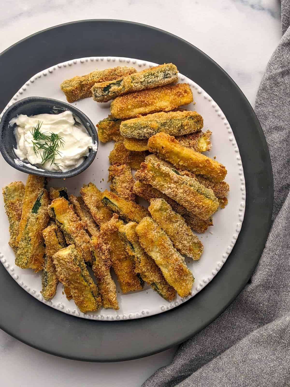 Healthy zucchini fries served on a white plate with a yogurt and dill dip.