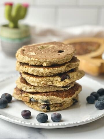 Blueberry oat pancakes on white plate next to blueberries.