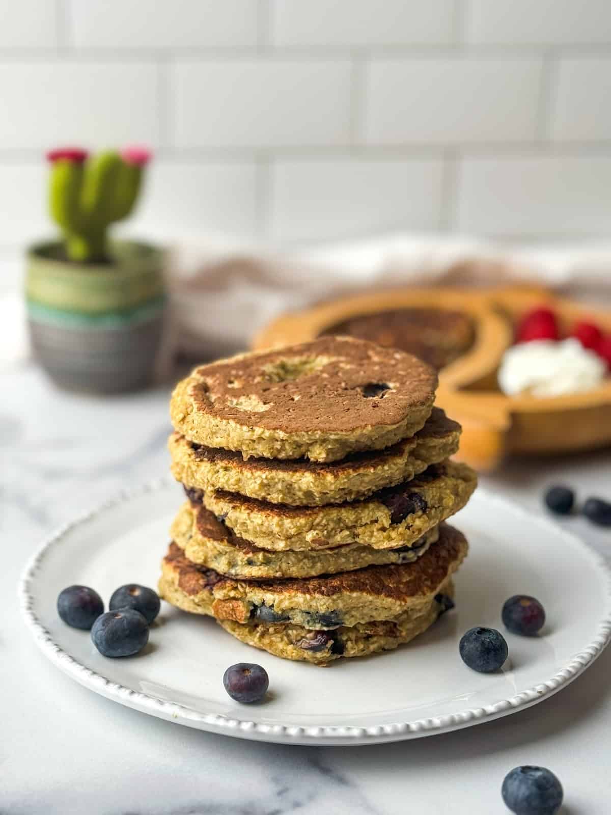 Stack of blueberry oatmeal pancakes on a white plate next to blueberries.
