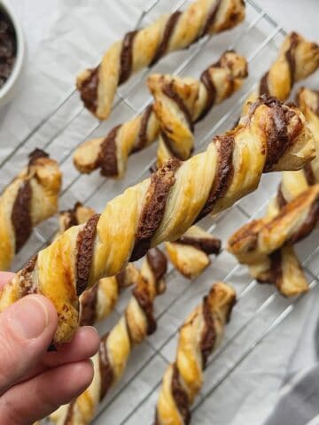 Holding chocolate twist when they come out of the oven with a rack with chocolate twists at the back.