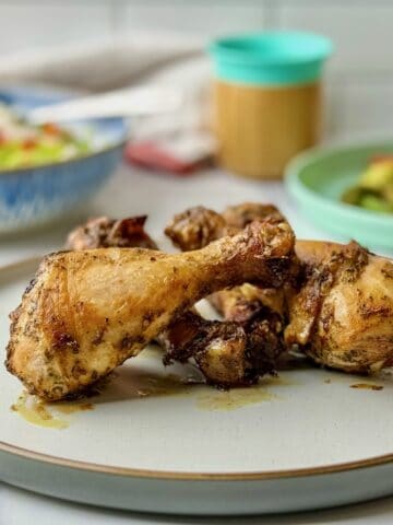 Paprika chicken drumsticks served on a plate next to salad and plate with serving for kids.