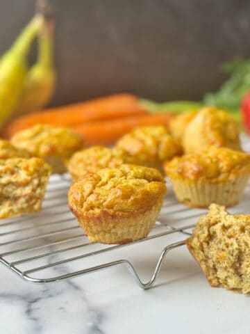 ABC muffins on a rack with bananas, carrots and apple at the back.