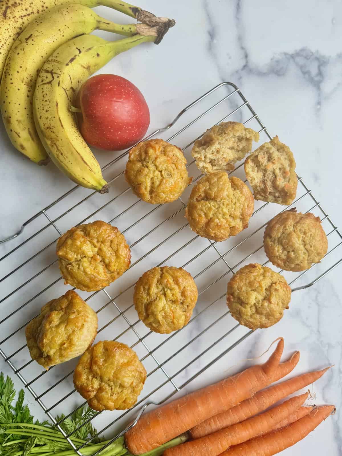 ABC muffins on a rack next to bananas, carrots and apple.