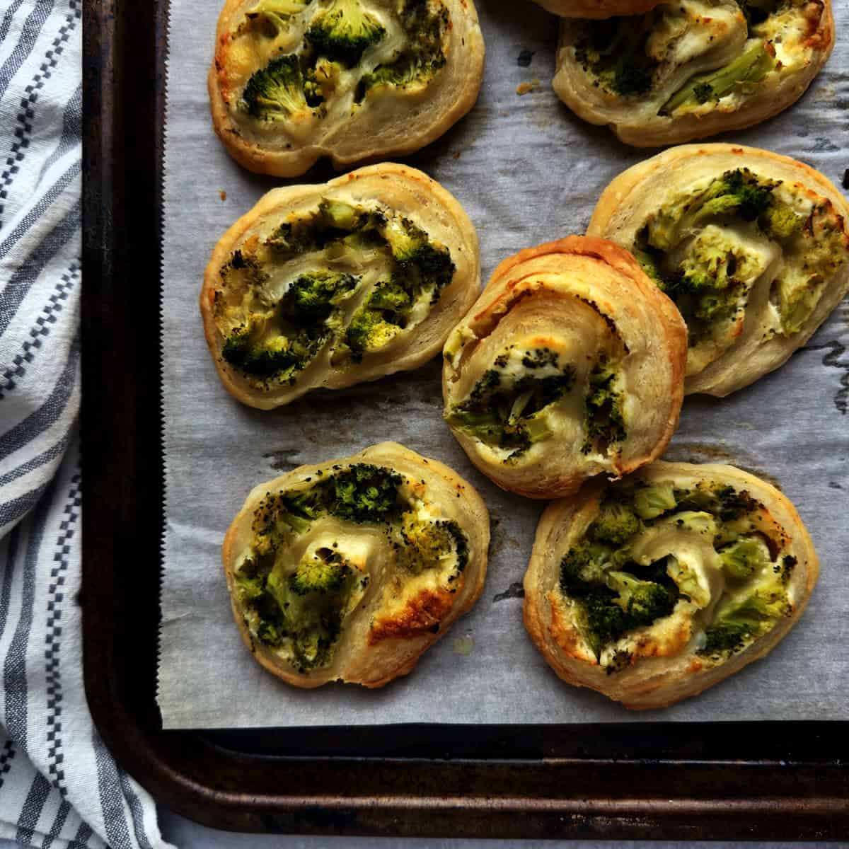 Broccoli and cheese pinwheels on a lined baking tray.