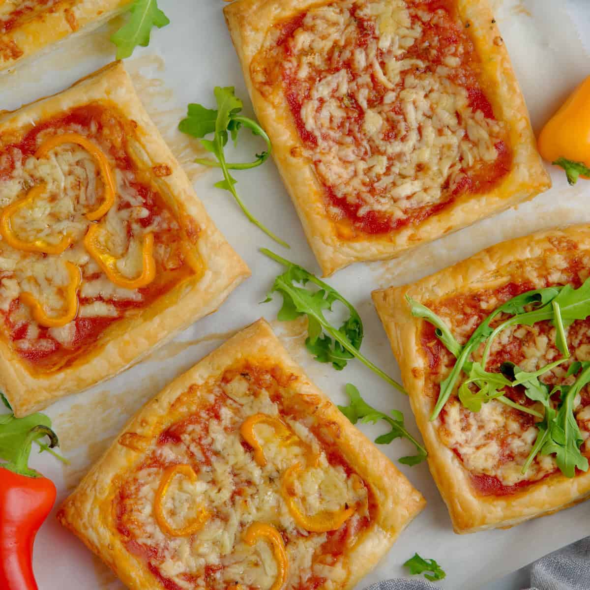 Puff pastry mini pizzas on the table with peppers and arugula leaves between them.