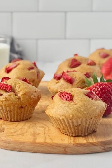 Strawberry cottage cheese muffins on a wooden board next to strawberries and a glass of milk.
