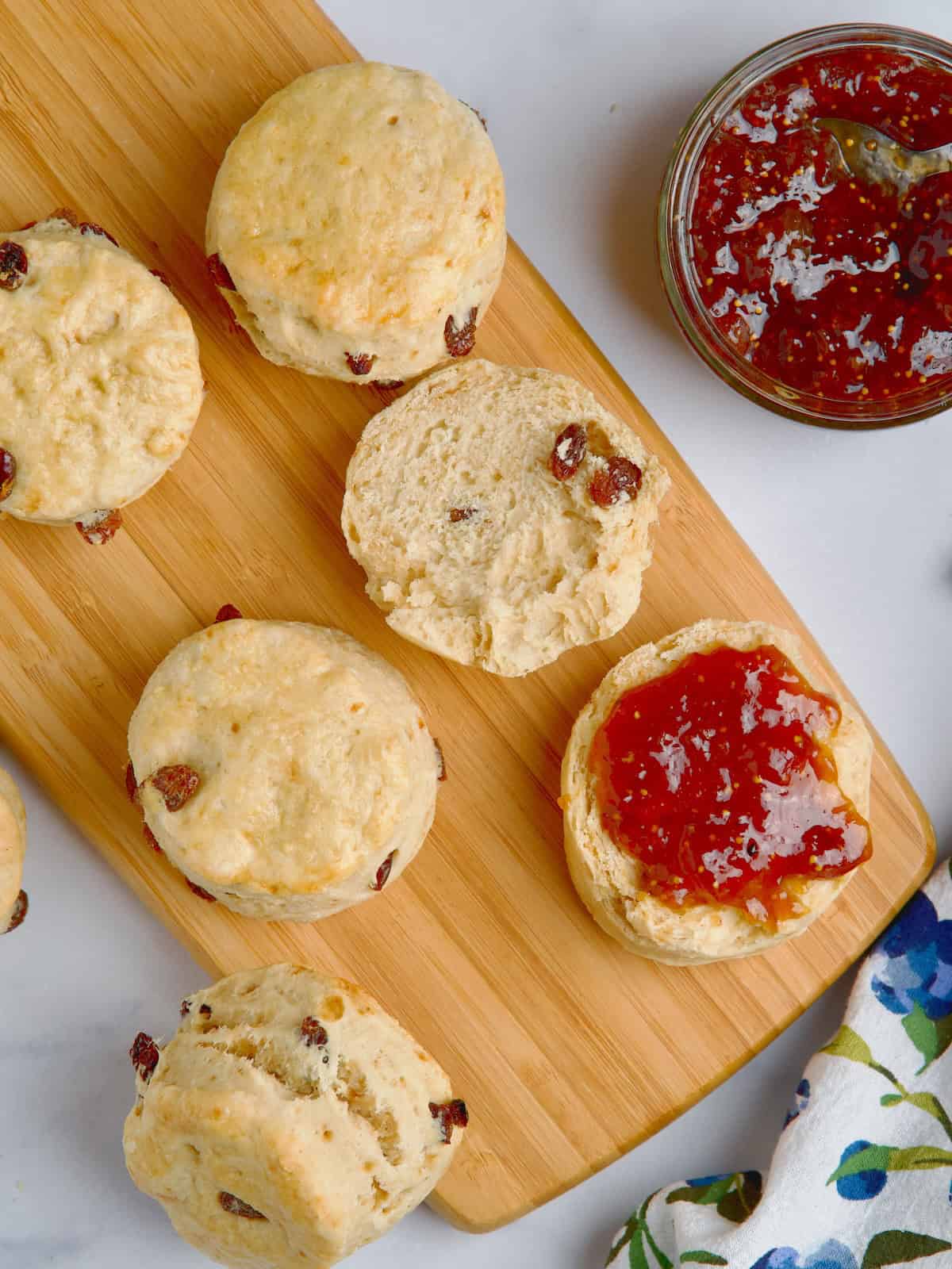 Fruit scones on a wooden board next to a jar with jam.