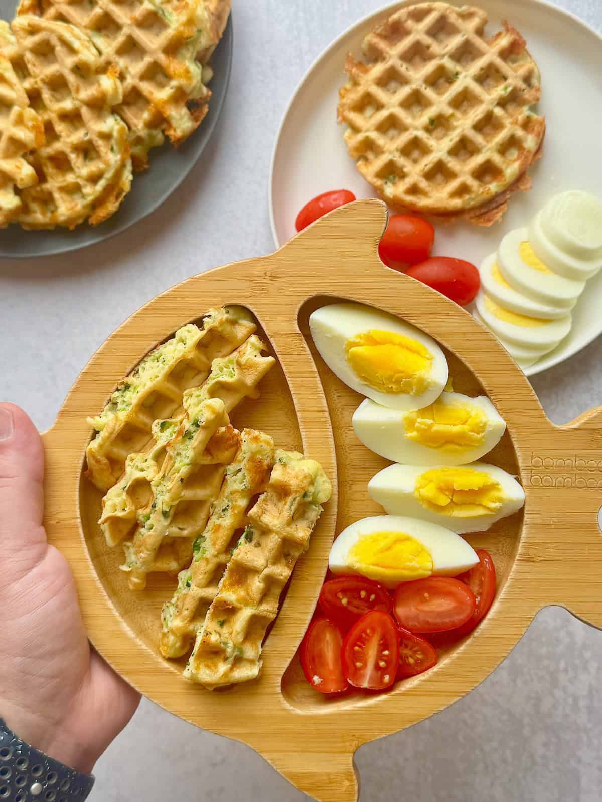 Zucchini cheese waffles on bamboo plate next to tomatoes and boiled egg.