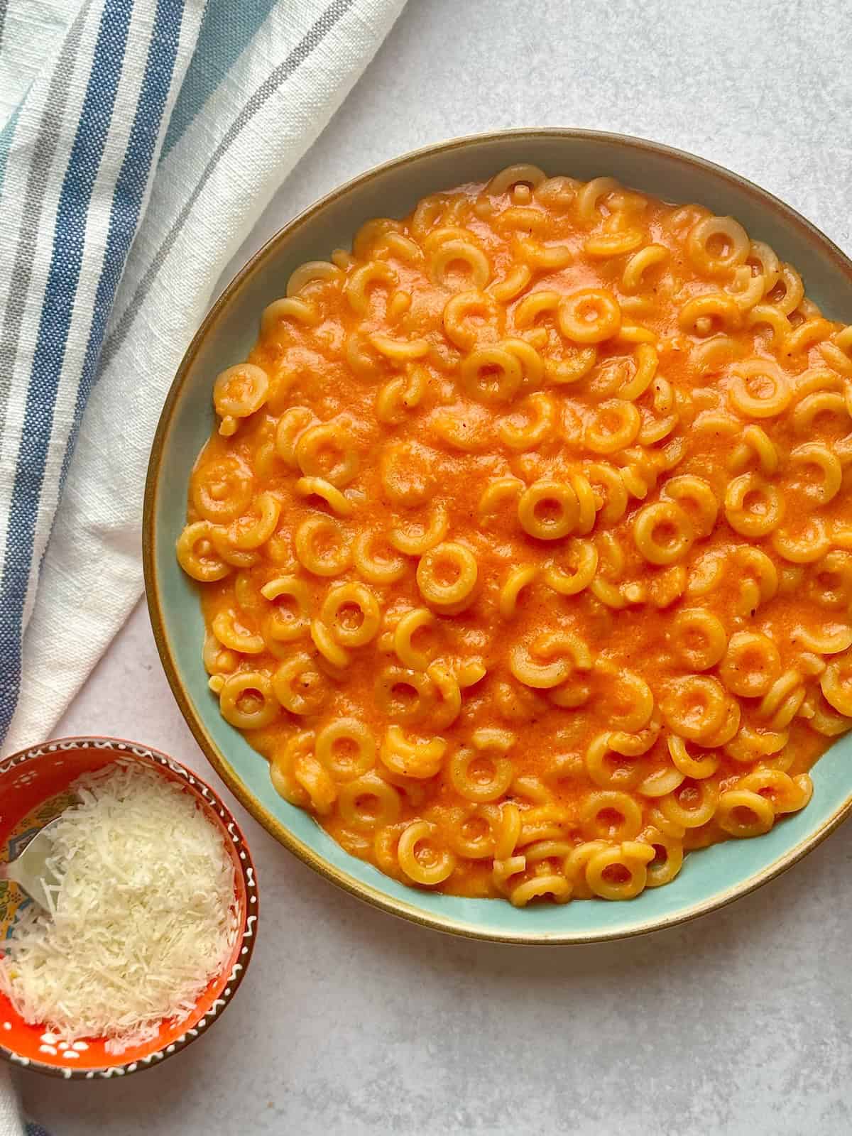 Homemade spaghettios served in a blue plate next to bowl with parmesan cheese.