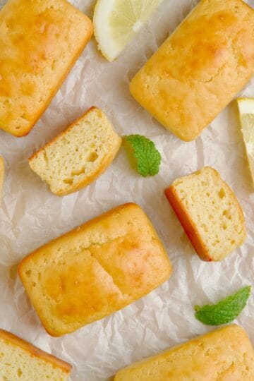 Mini lemon loaf cakes on a board next to slices of lemon and mint leaves.