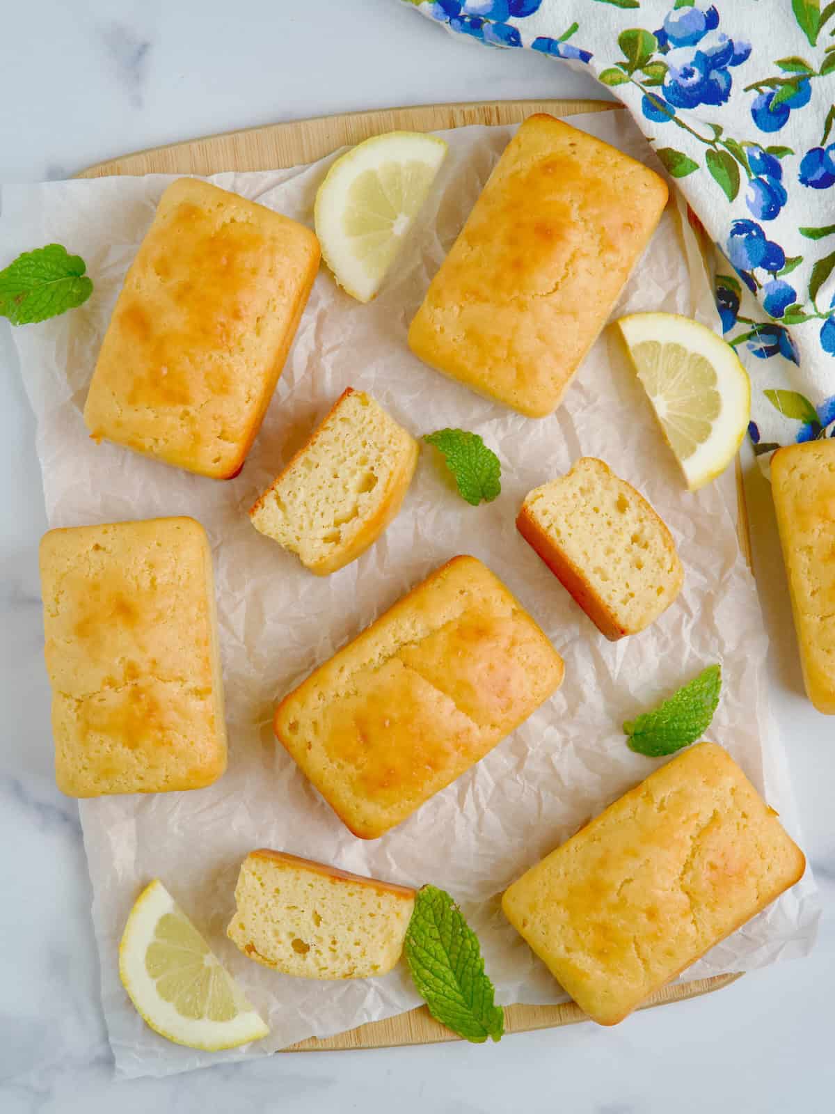 Mini lemon loaf cakes on a board next to slices of lemon and mint leaves.