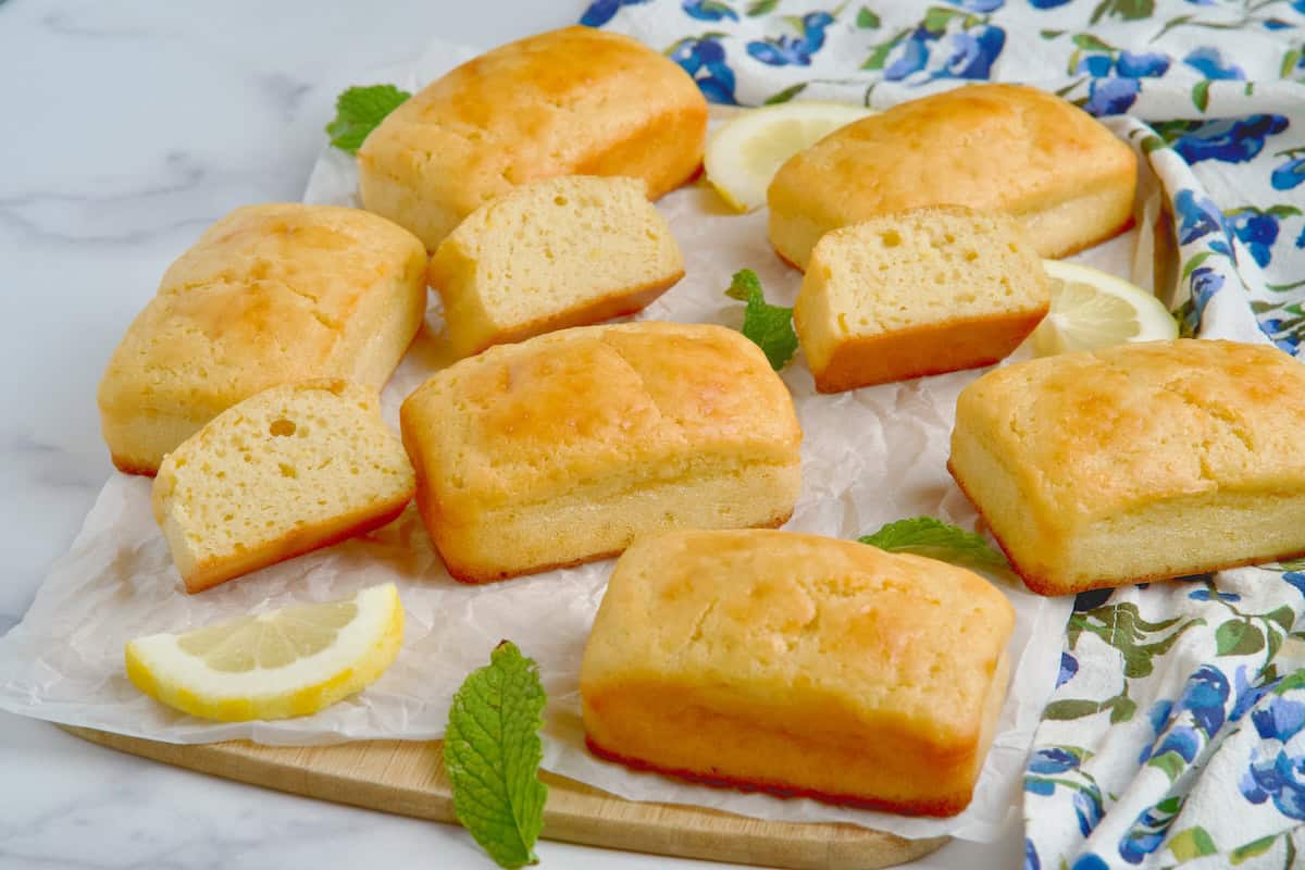 Mini lemon loaf cakes on a wooden board next to lemon slices.