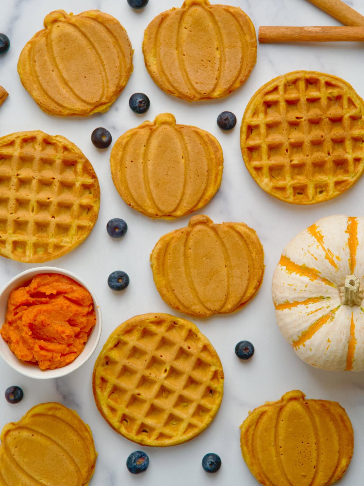 Pumpkin spice waffles in different shapes next to squash and bowl with pumpkin purée.