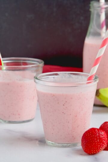 Strawberry banana smoothie in two glasses next to strawberries and bananas.
