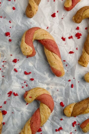 Candy cane cookies on a parchment paper with dried raspberries between them.