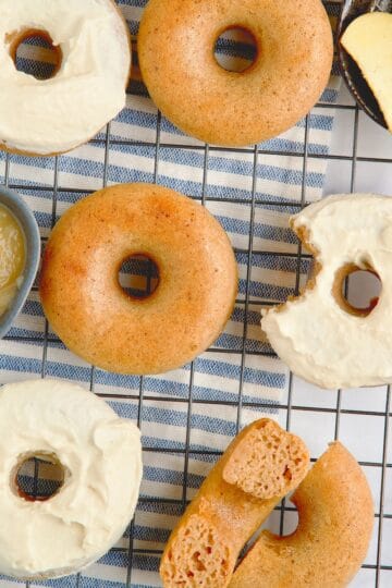 Apple cinnamon donuts on a wire rack with some having frosting on top.