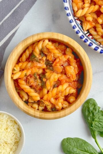 Pasta with tuna and spinach tomato sauce served in a wooden bowl.