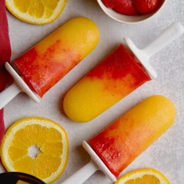 Orange mango popsicles with orange slices, strawberries and mango cubes in between.