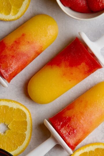 Orange mango popsicles with orange slices, strawberries and mango cubes in between.