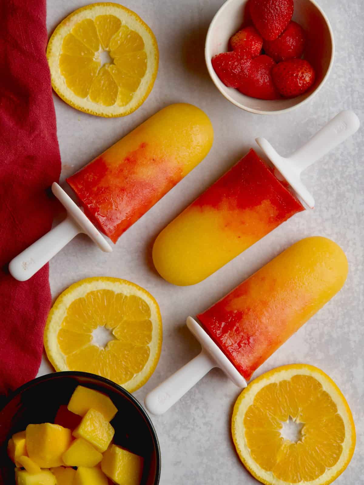 Orange mango popscicles with orange slices, strawberries and mango cubes in between.