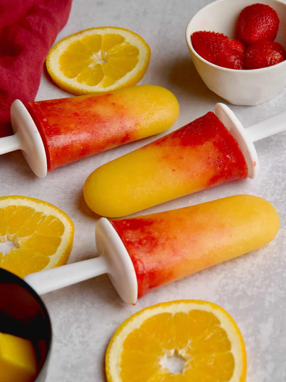 Orange and mango sunrise popsicles with orange slices between them.