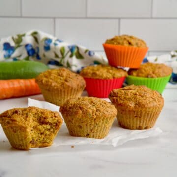 Morning glory muffins on the table with a zucchini and a carrot in the background.