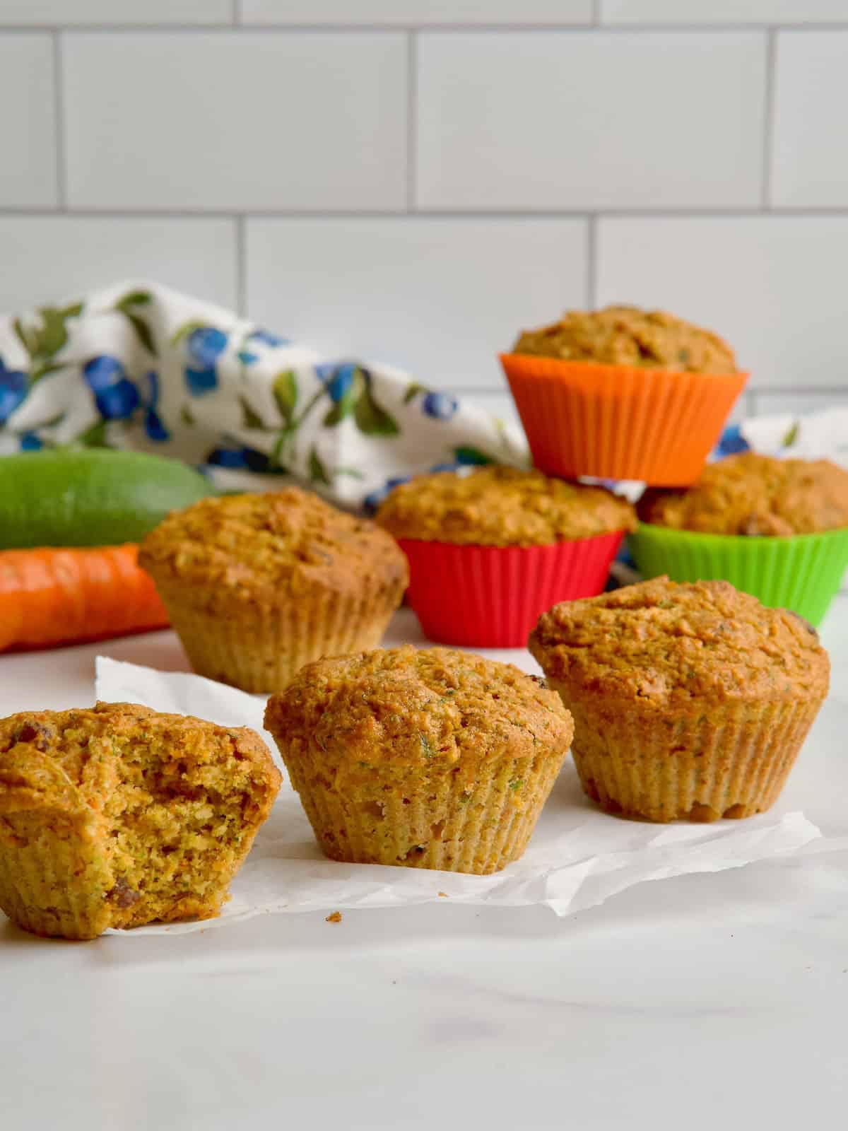 Morning glory muffins on the table with a zucchini and a carrot in the background.