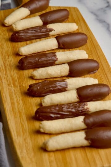 Half covered chocolate cookie sticks on a board next to each other.