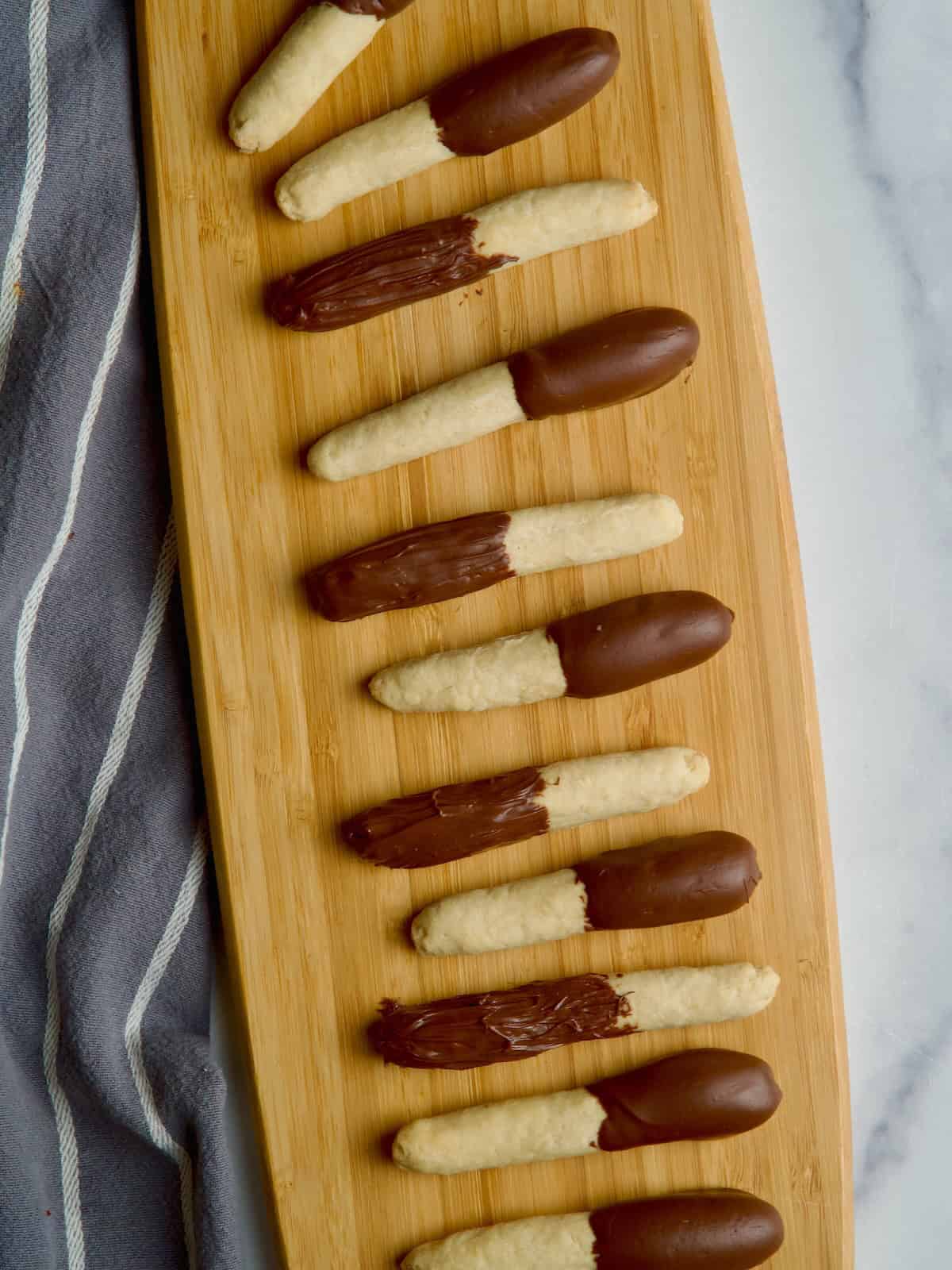 Half covered chocolate cookie sticks on a board next to each other.
