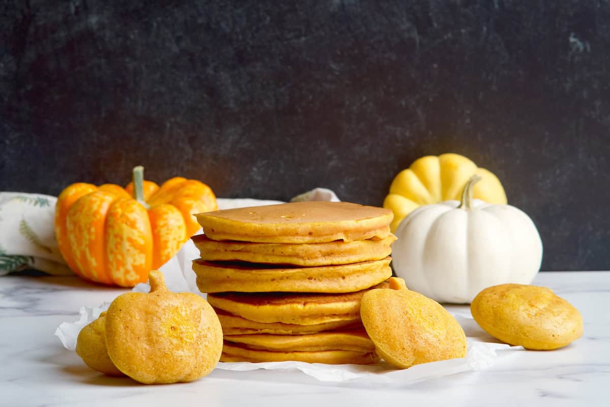 Pumpkin pancakes stack next to pumpkin shaped pancakes.