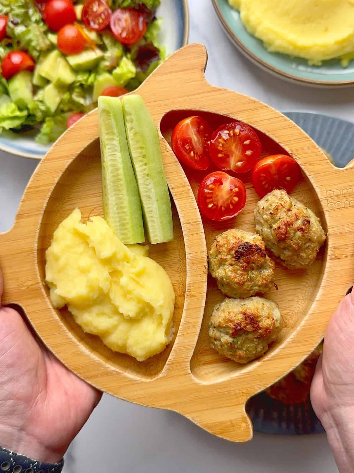 Turkey zucchini meatballs served on bamboo plate with mashed potatoes, cucumber sticks and tomatoes.