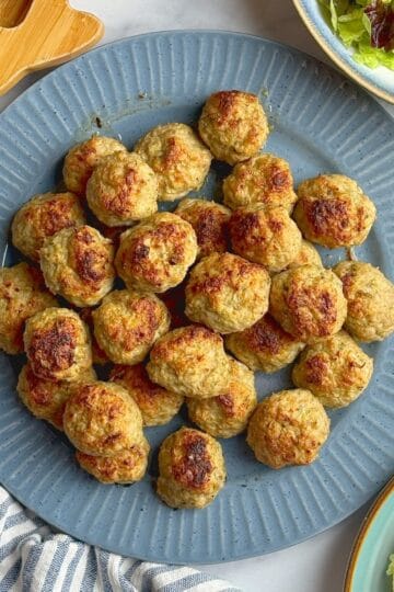 Turkey zucchini meatballs on a blue plate next to salad bowl.