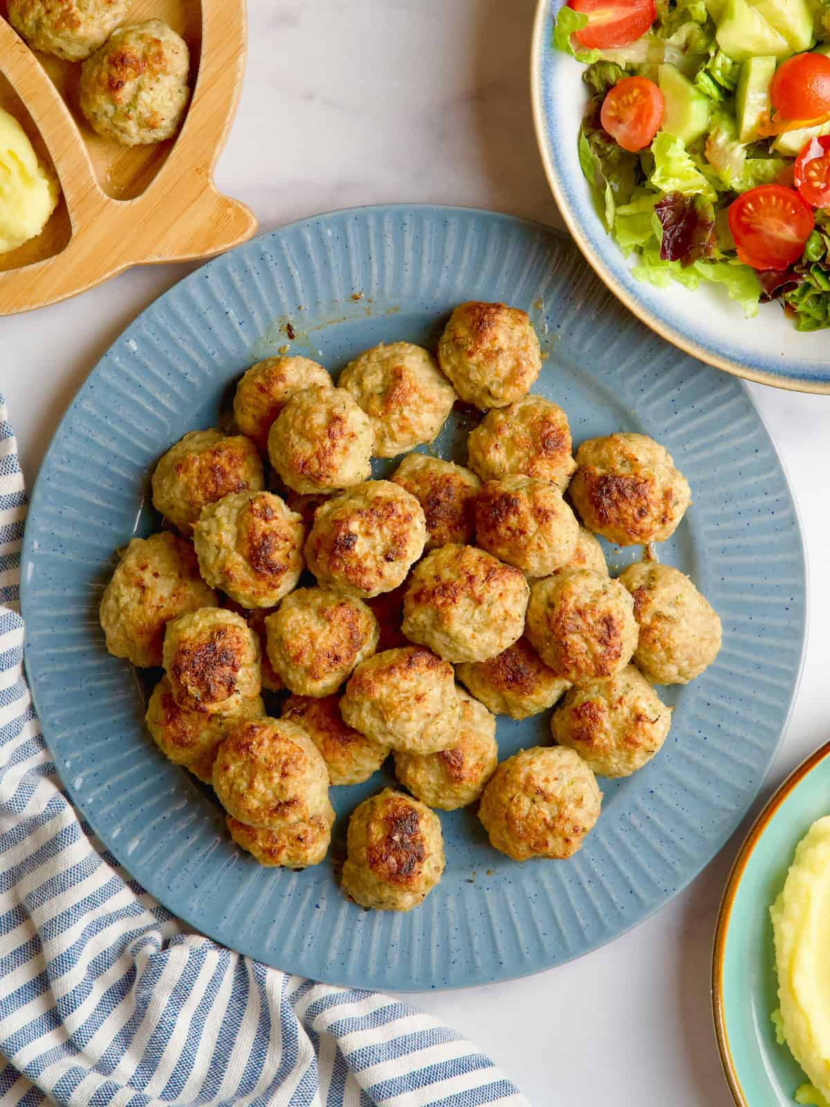 Turkey zucchini meatballs on a blue plate next to salad bowl.